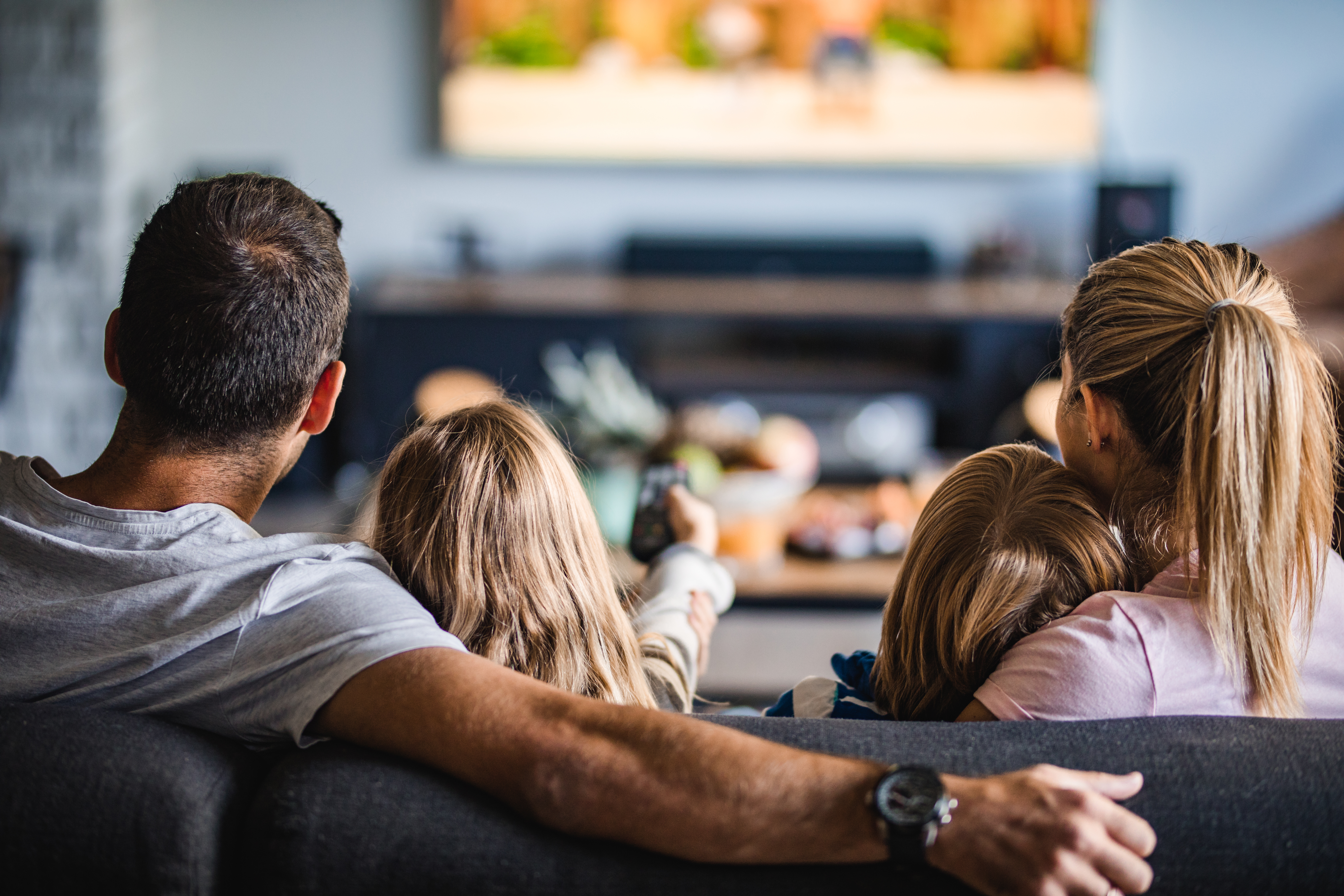 Back view of a relaxed family watching TV on sofa in the living room